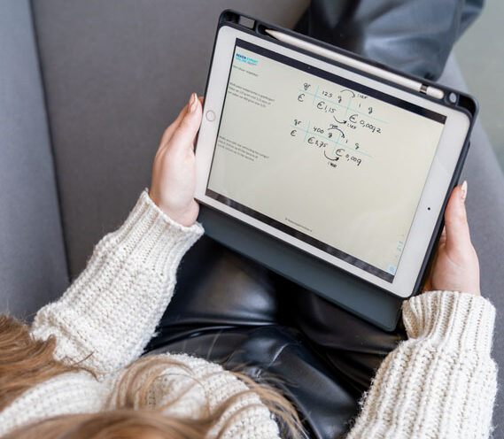 Pabo student met een witte trui en zwarte broek zit achter een ipad. Ze leer hiermee voor sommen voor de kennisbasis toets rekenen.
